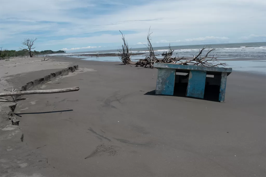 Entre la arena yacen restos de antiguos edificios arrastrados hacia el mar. En la imagen, lo que perdura de una caseta de baños pintada de azul. Fotografía: Alexander Campos Sandoval.