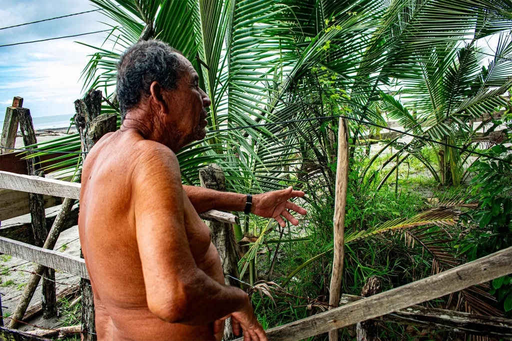 Junto a lo que queda de su huerta, Reducildo Reina explica cómo el territorio se ha ido con el mar, que amenaza de fondo. Fotografía: Manuel José Cárdenas Martínez.