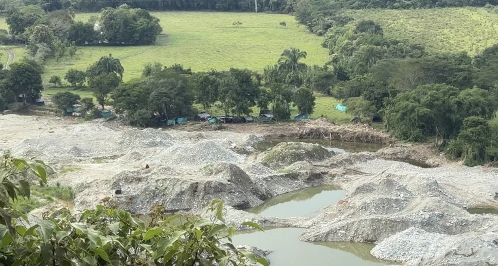 Vista panorámica de uno de los frentes de explotación sobre el río Saldaña. Los montículos de material extraído y las charcas de agua contaminada contrastan con los potreros verdes del fondo, donde carpas improvisadas alojan a trabajadores llegados de otras regiones del país.